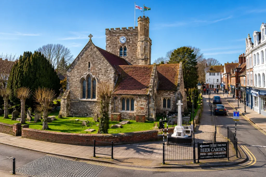 Professional view of St Faith’s Church in Havant, showing the historic stone church, clock tower, churchyard, war memorial, nearby high street and sunny blue sky.