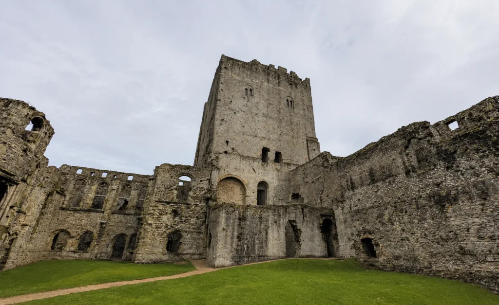 Interior view of Portchester Castle, showing the historic stone keep, ruined castle walls, arched openings, grass courtyard and overcast sky.