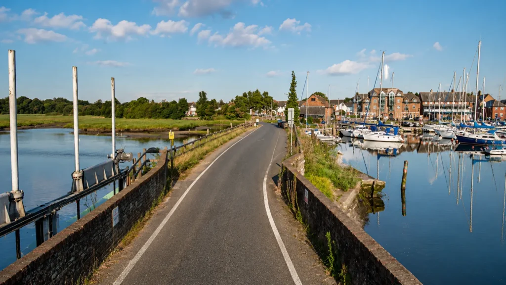 Professional view of Eling Toll Bridge in Totton, showing the narrow road across the water, brick bridge walls, marina boats, riverside greenery and calm reflections on a sunny day.