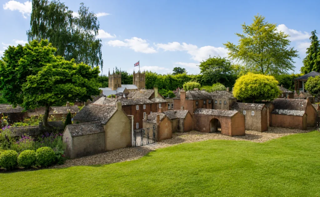 Professional view of Wimborne Model Town, showing miniature buildings, small streets, garden landscaping, trees and the model Minster towers under a bright blue sky.