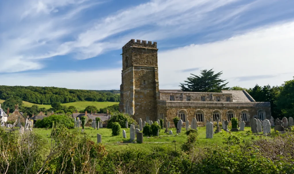 Abbotsbury Abbey remains and churchyard set against green Dorset countryside and rolling hills.