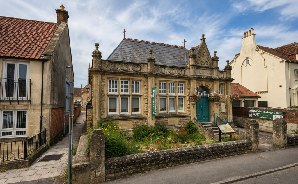 Calne Heritage Centre with its historic stone frontage, flower garden and surrounding town buildings.