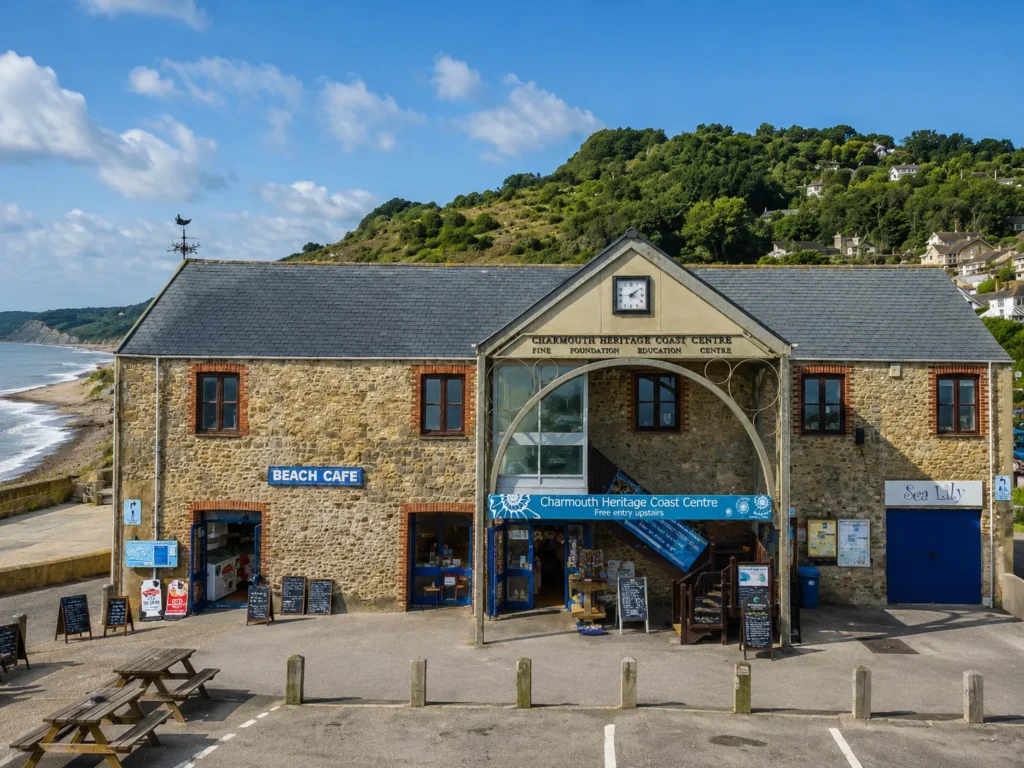 Charmouth Heritage Coast Centre by the seafront with the Jurassic Coast cliffs and green hillside in the background.