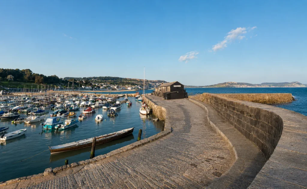 Lyme Regis harbour with boats moored beside the Cobb and coastal cliffs in the distance.