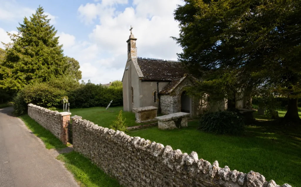 St Francis' Church in Maiden Newton, Dorset, surrounded by a stone wall, greenery and mature trees.